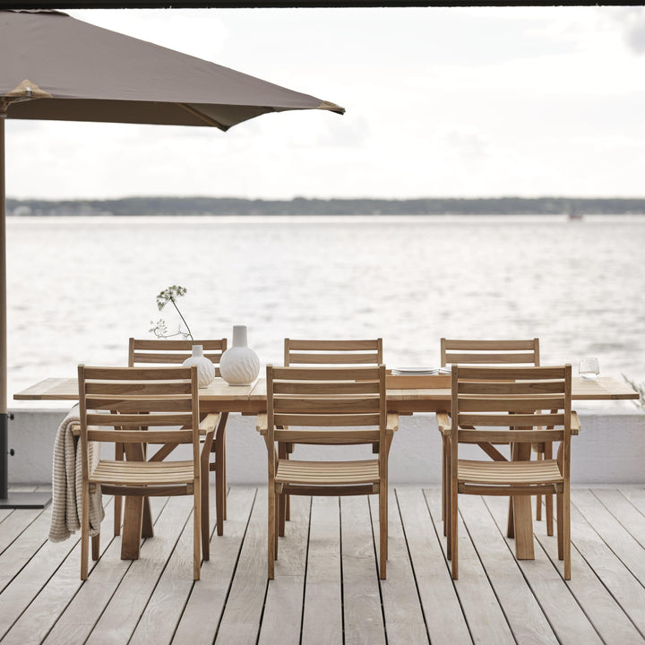 Brafab Keros spisestol i teak ved langbord på terrasse ved sjøen under parasoll