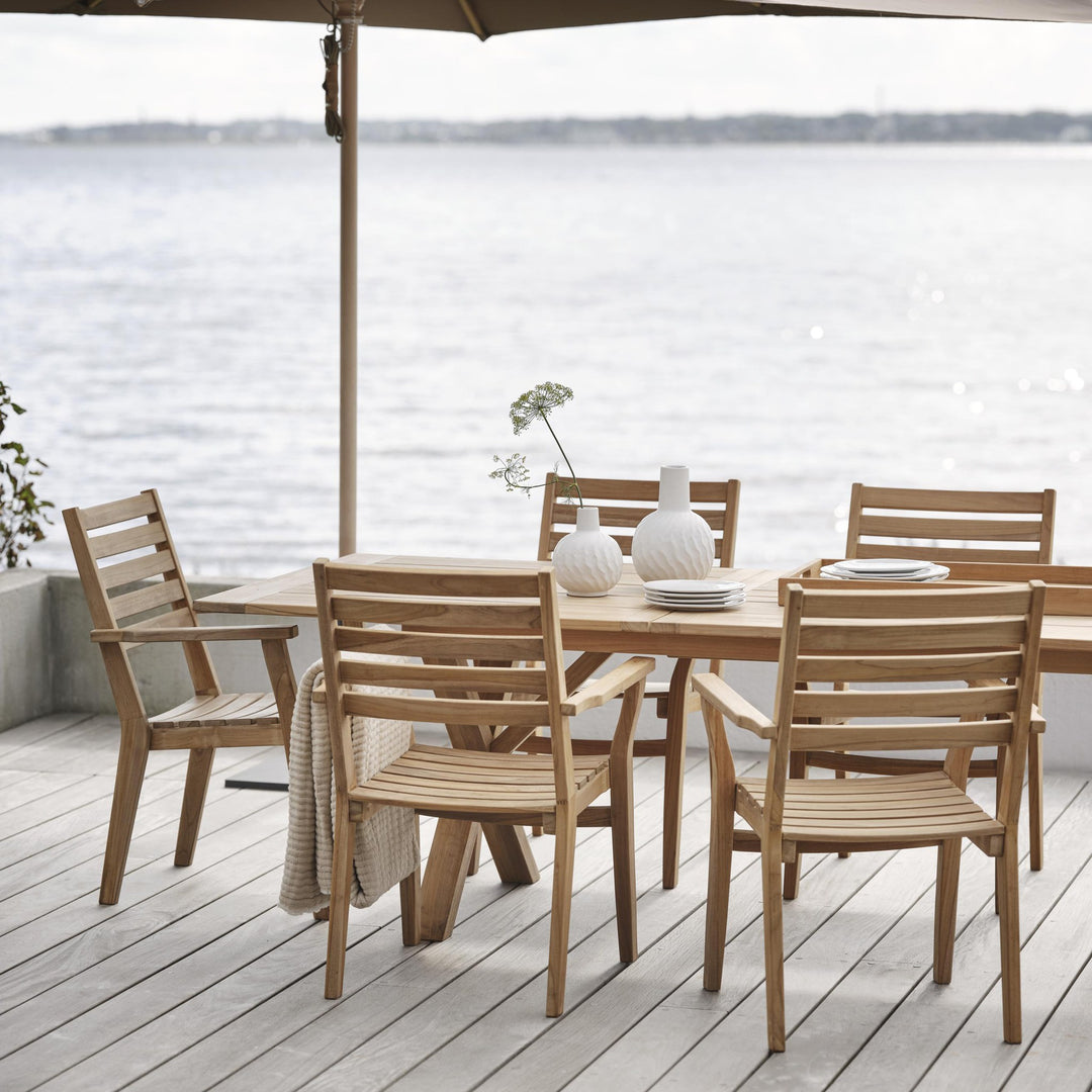 Brafab Keros spisestol i teak med bord på terrasse ved sjøen under parasoll