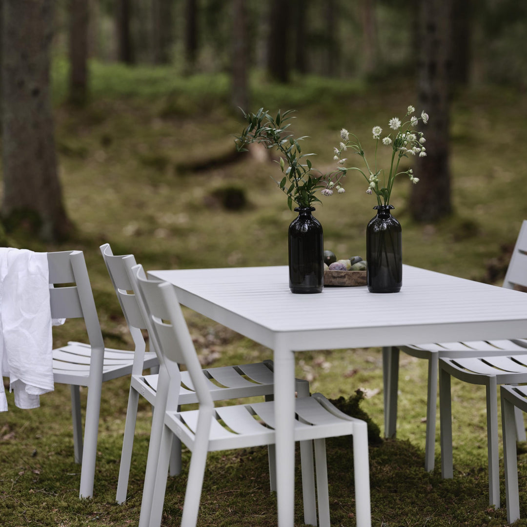 Brafab Delia spisestol uten armlene i lys grå ved bord i skog med mørke vaser og blomster