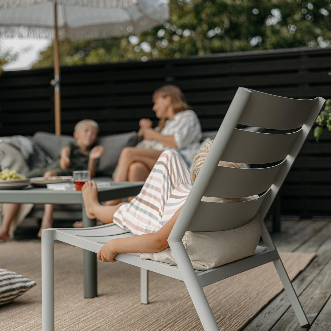 Brafab Delia loungestol i lys grå med pute på terrasse, barn sitter i stolen, familie bak