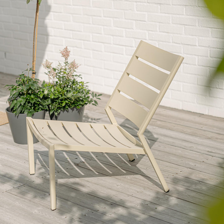 Brafab Delia loungestol i lys gul aluminium på terrasse med planter og hvit murvegg