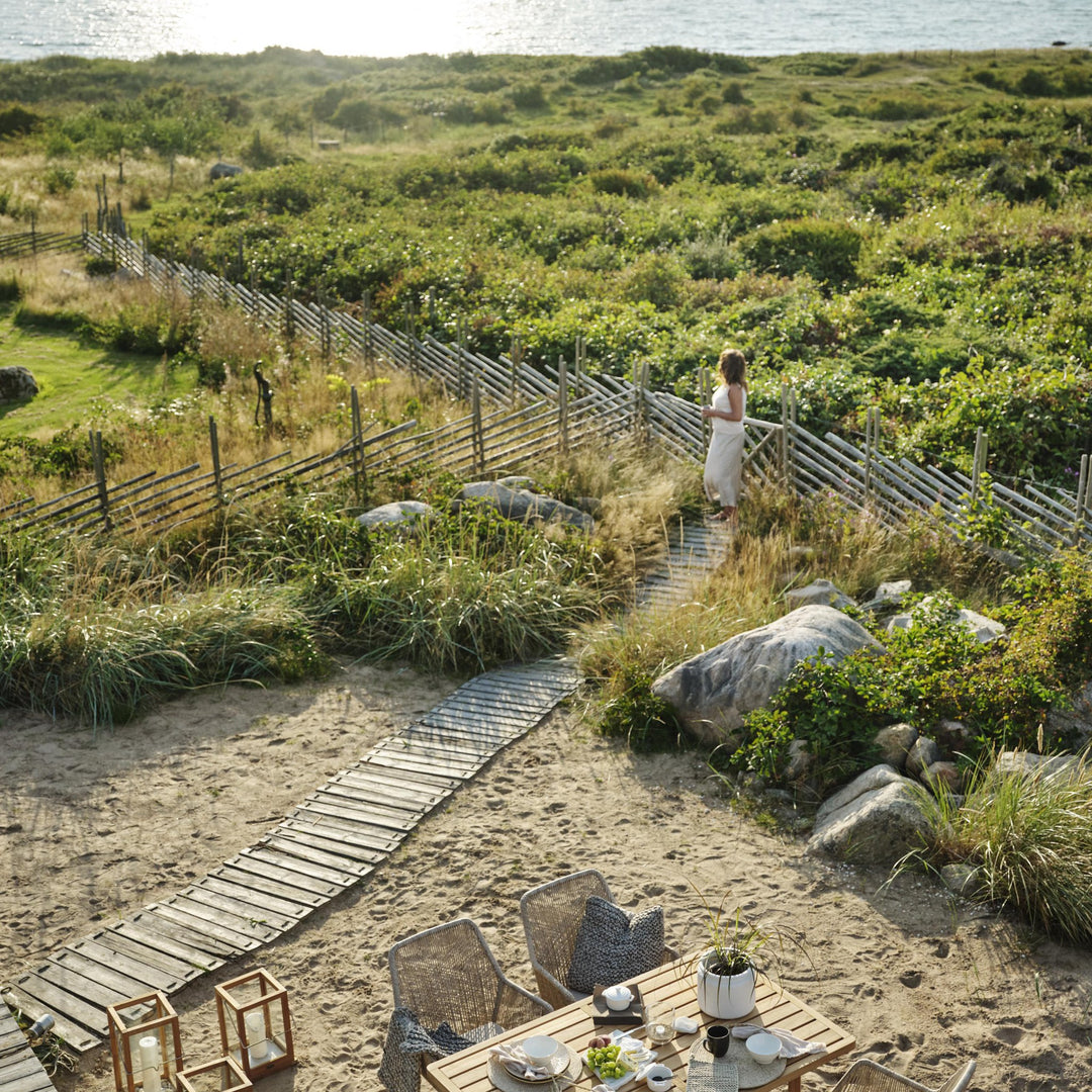 Brafab Midway spisegruppe i teak på strand med kystlandskap og sjø i bakgrunnen