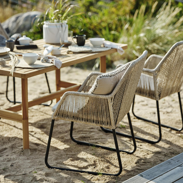 Brafab Midway spisestol i beige tau ved trebord på stranden med dekket bord