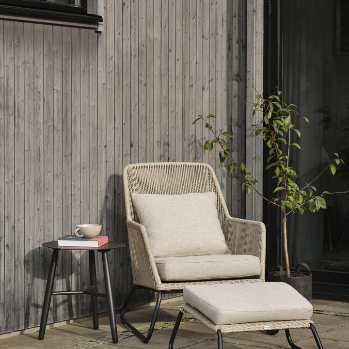 Brafab Midway loungestol i beige på terrasse, sidebord med kopp og bøker, plante og fotskammel
