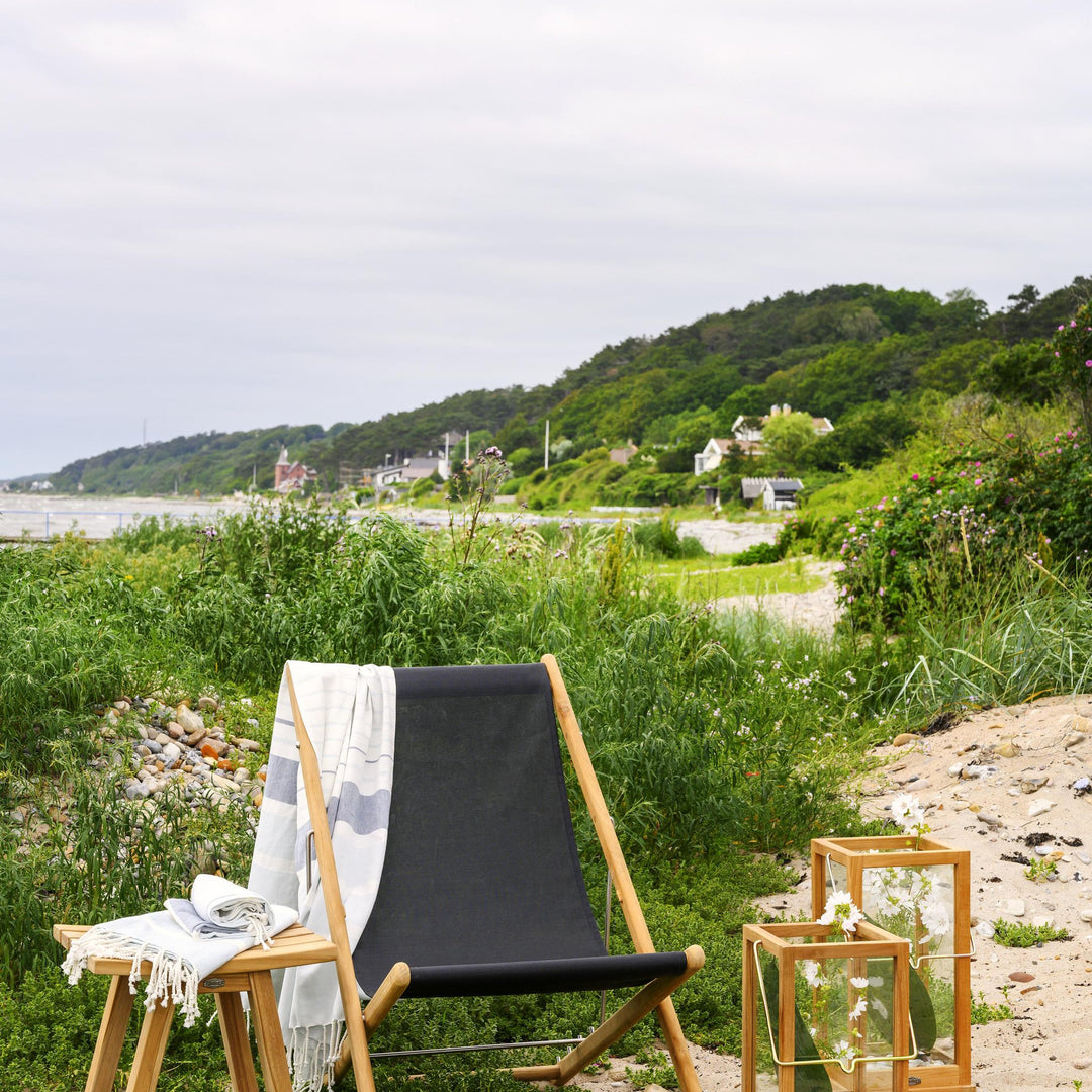 Brafab Keros krakk i teak ved stranden, brukt som sidebord med pledd, kystlandskap bak