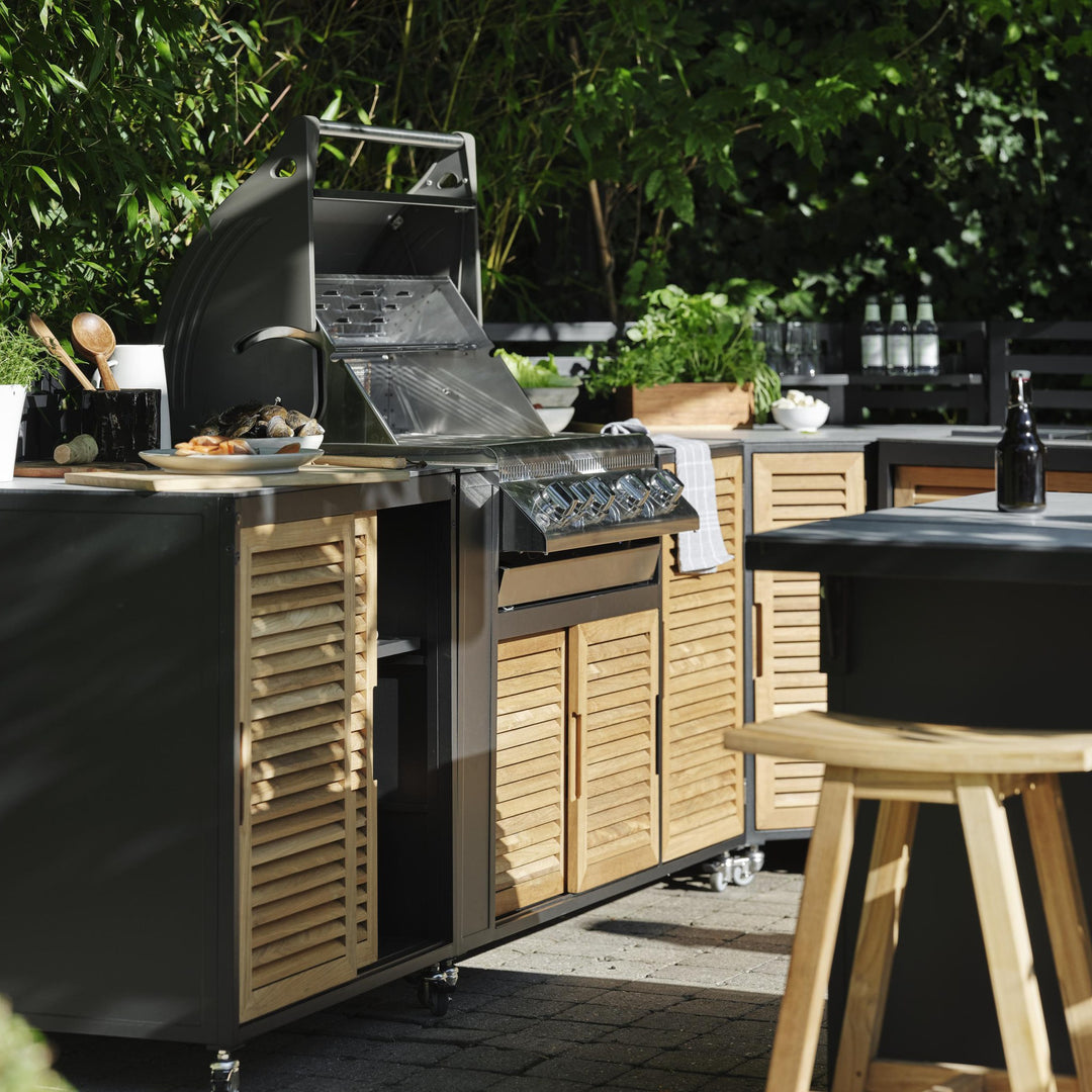 Brafab Keros barstol i teak ved svart utekjøkken med grill i hage, omgitt av grønt