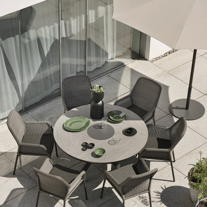 Brafab Dimma spisestol i mørk grå flettverk ved rundbord på terrasse, med parasoll og grønt servise.