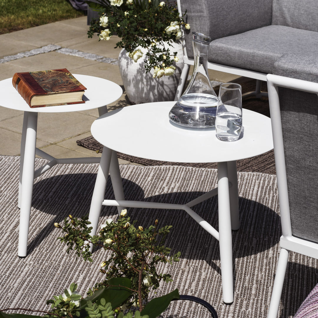 Brafab Vannes sofabord i hvitt på uteteppe ved hvit loungesofa, med bok, glasskaraffel og roser.