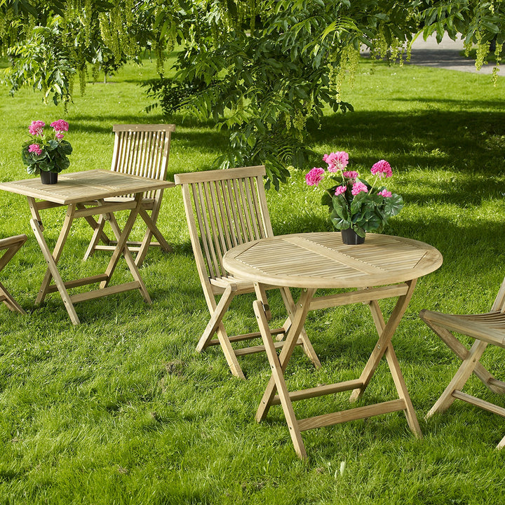 Brafab Turin spisebord i teak med klappstoler på plen under tre, rosa pelargonia i potte