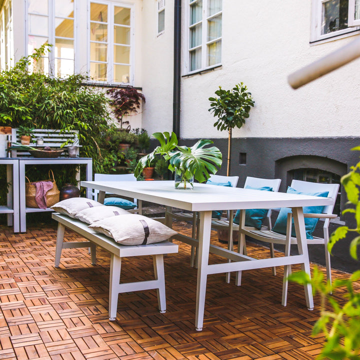 Brafab Vevi spisebord i hvitt på bakgård med terrakottafliser, med benk, blå puter og grønne planter.
