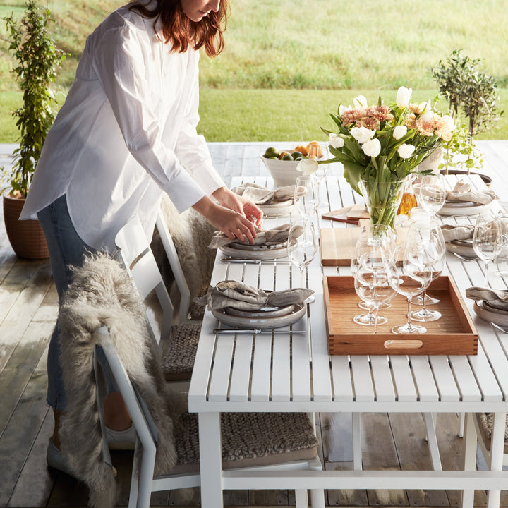 Brafab Vevi spisebord i hvit, kvinne dekker bordet med saueskinn, tulipaner og vinglass på terrasse