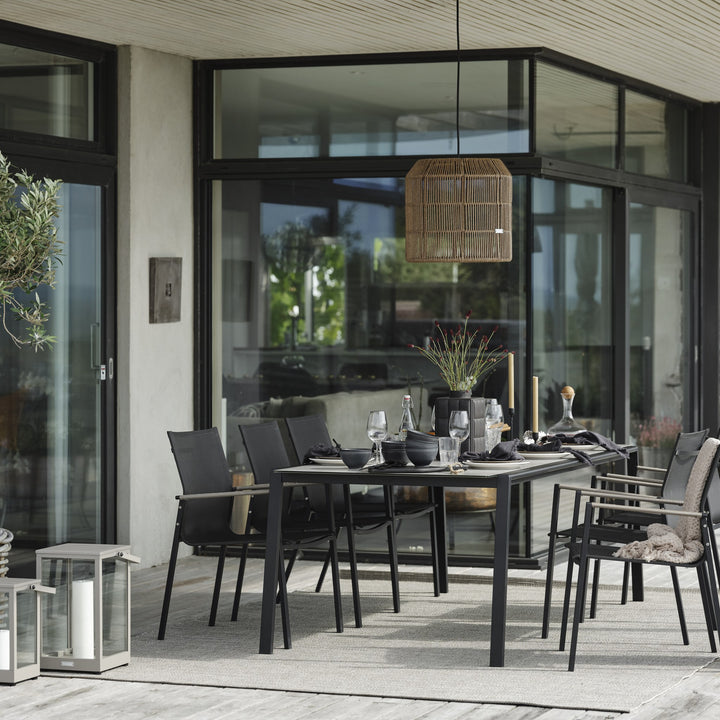 Brafab Lyra spisebord i mørk grå med sorte tekstilstoler på terrasse, under flettet pendellampe.
