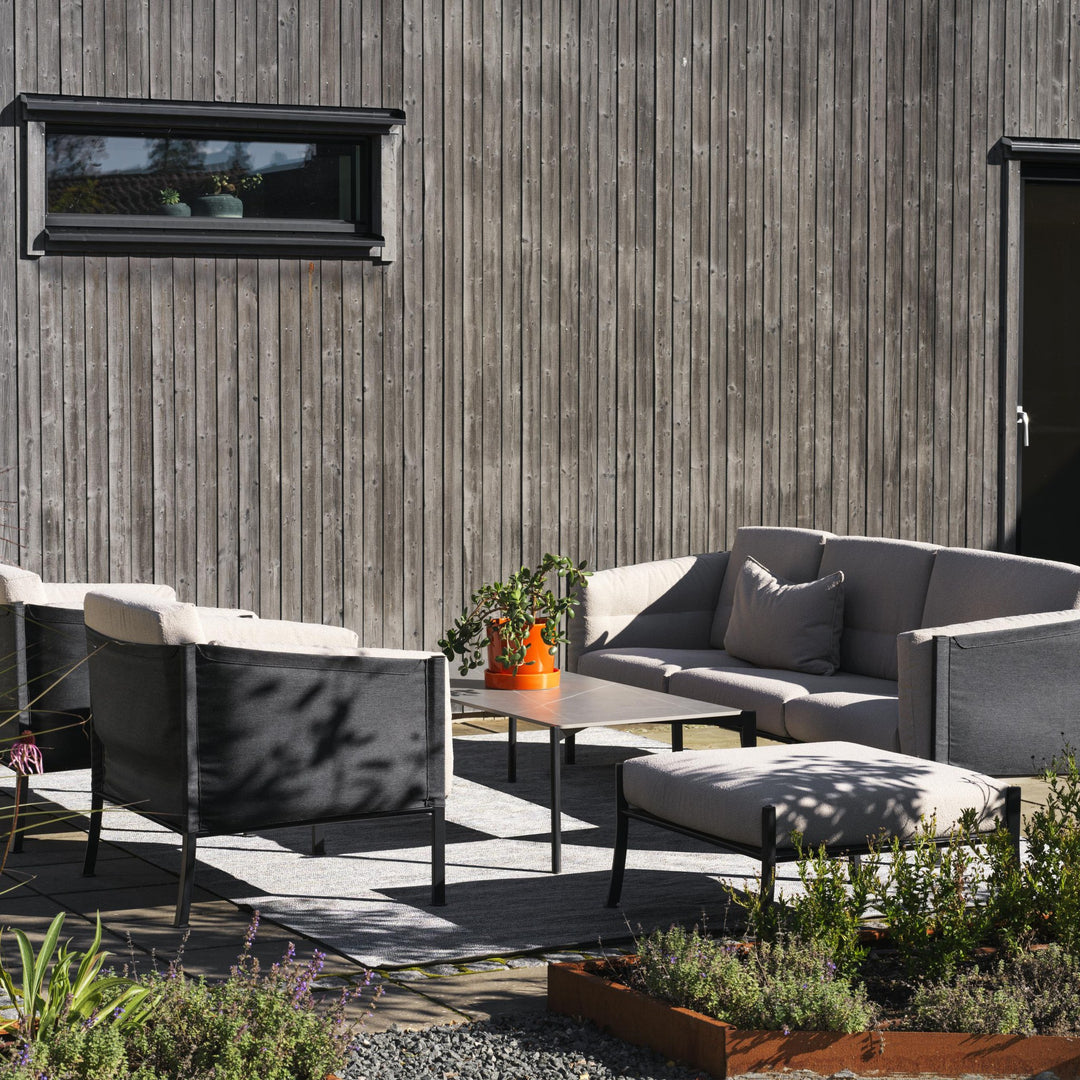 Brafab Hallavara sofabord i grå med spileplate i loungegruppe på terrasse, foran værbitt trefasade.