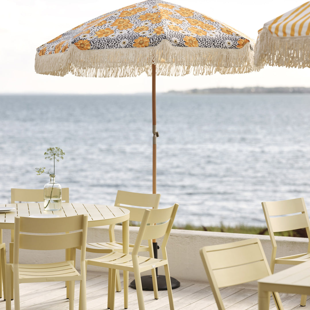 Brafab Bigby spisebord i lys gul med stoler på terrasse, blomstrete parasoll og sjøutsikt