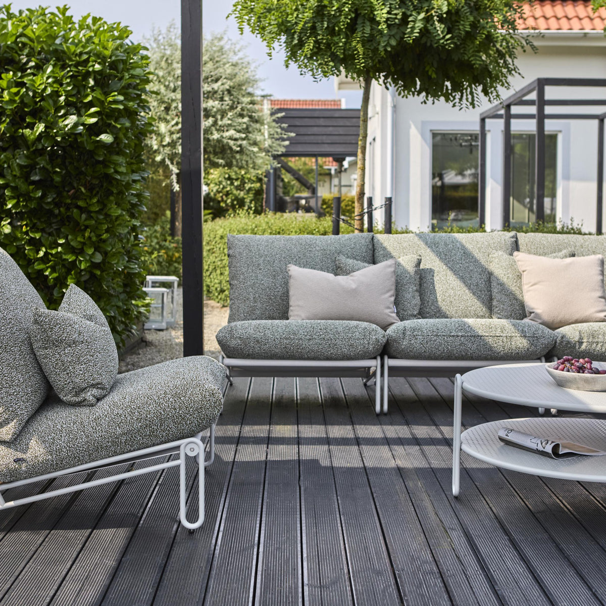 Brafab Blixt sofabord, lyst grått metallbord på tredekke med grågrønn loungesofa, puter og hekk bak