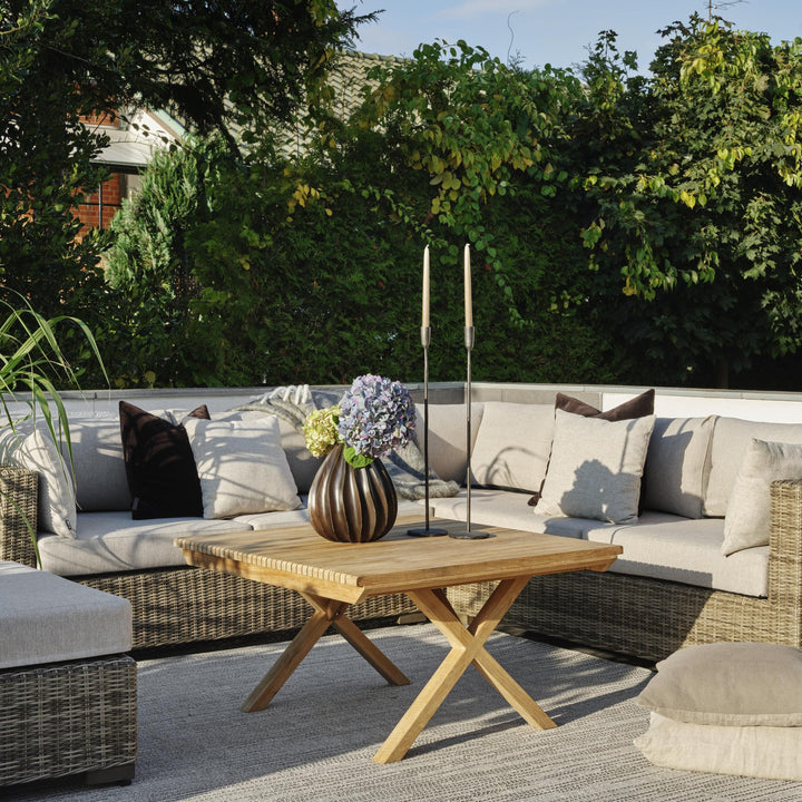 Brafab Julita sofabord i natur teak med blomstervase og lysestaker ved rottingsofa