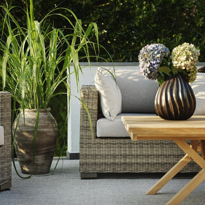 Brafab Julita sofabord i natur teak ved grå rottingsofa med gressplante og blomstervase