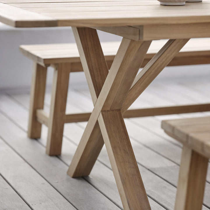 Brafab Brutus spisebord i natur teak, nærbilde av kryssben med benk på terrasse