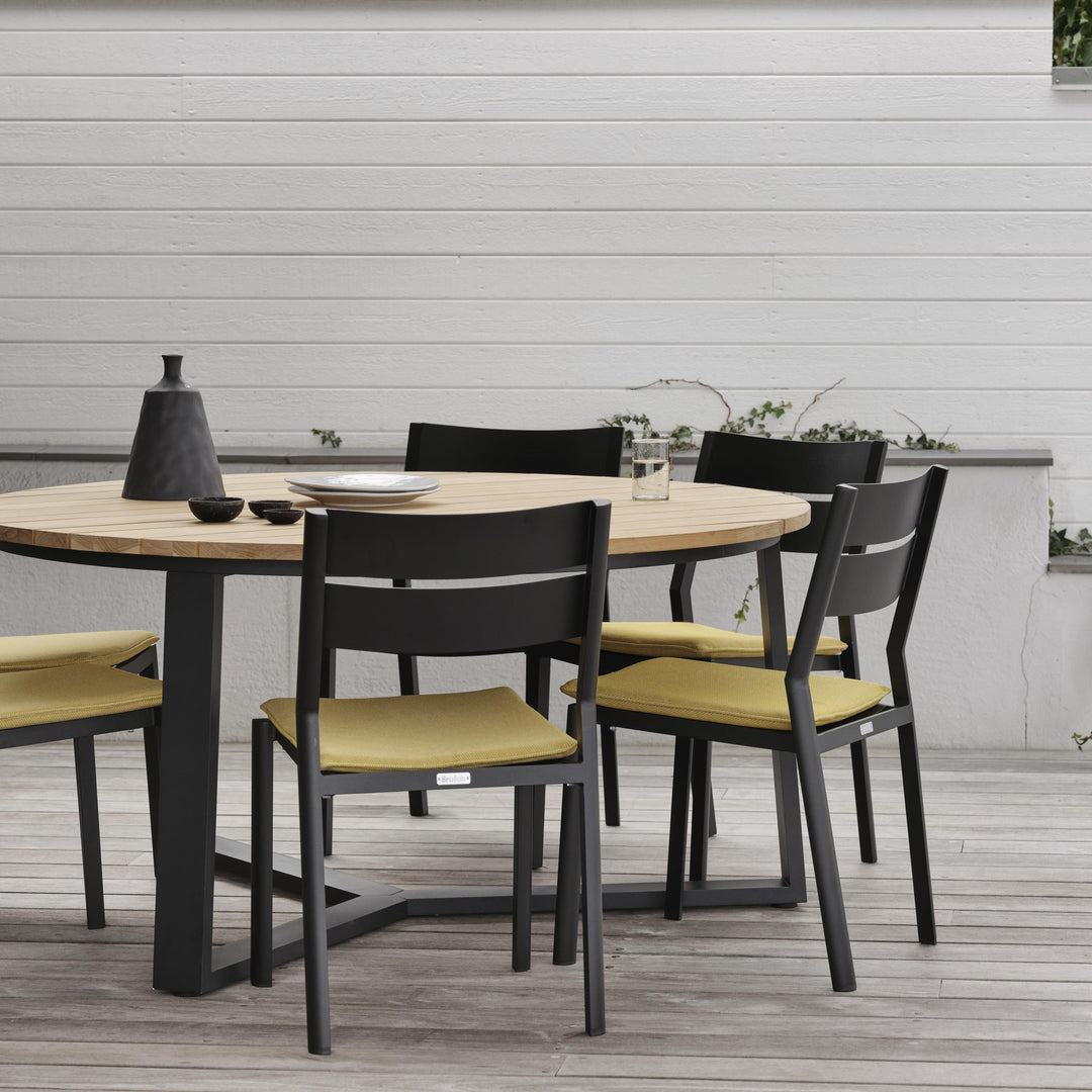 Brafab Laurion rundt spisebord i natur/sort med sorte stoler og gule puter ved hvitt hus
