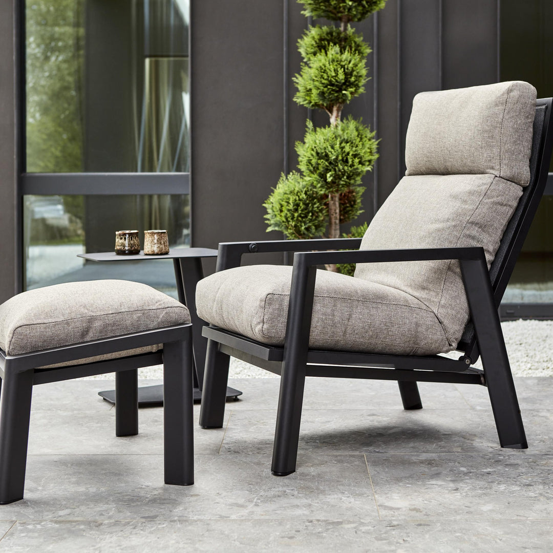 Brafab Slide sidebord i sort ved lenestol med beige puter og fotskammel, formklippet tre bak