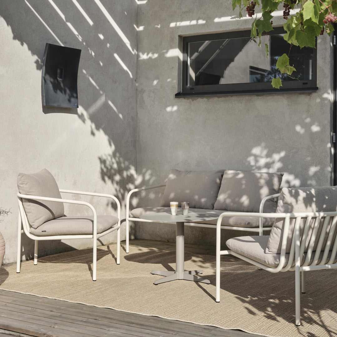 Brafab Mill sofabord, rundt i lys khaki, med kremhvit loungesofa på terrasse foran betongvegg