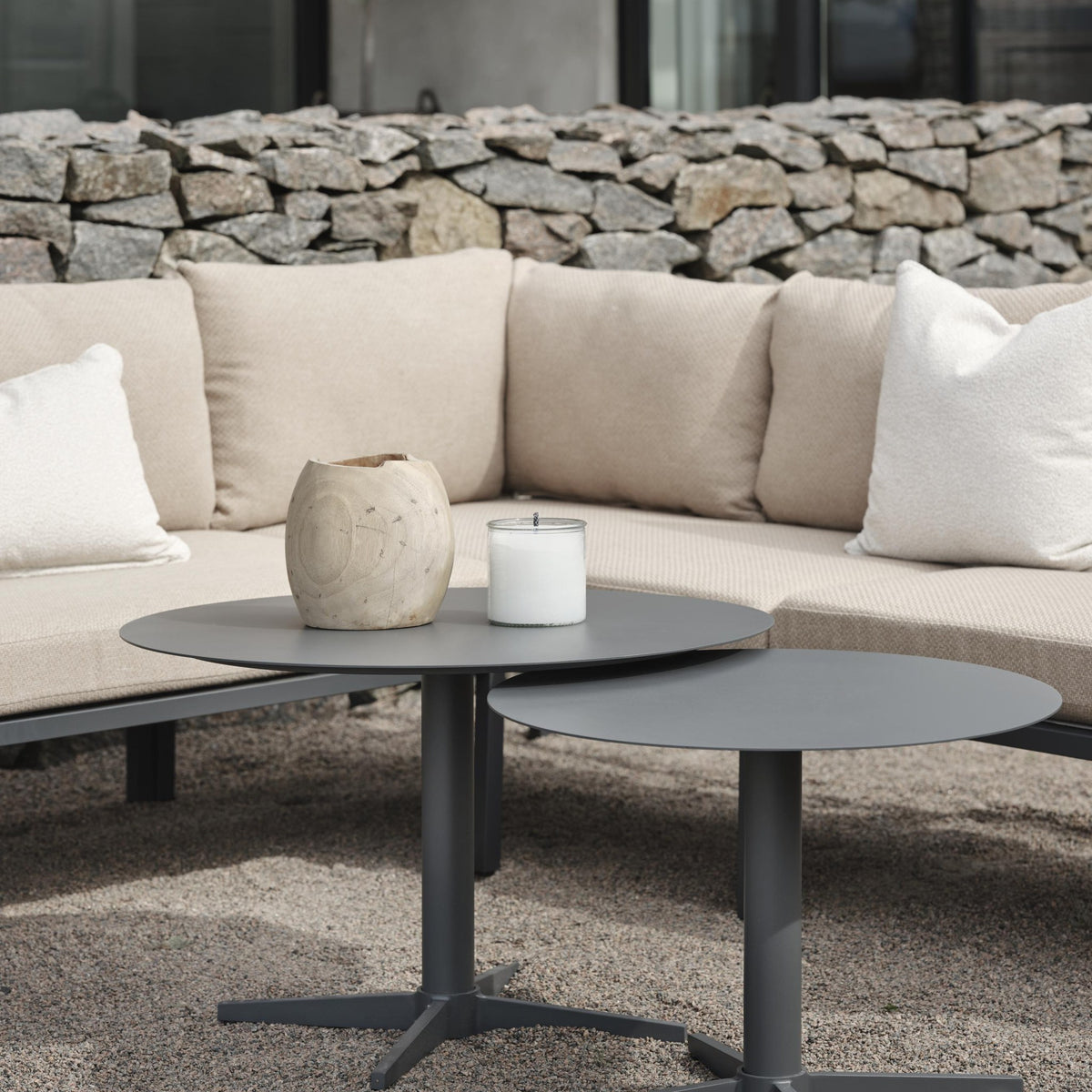 Brafab Mill sofabord, rundt i antrasitt, ved beige loungesofa foran steinmur, lys pute og lykt