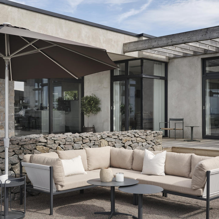 Brafab Mill sofabord i antrasitt foran beige utesofa på terrasse med parasoll og steinmur
