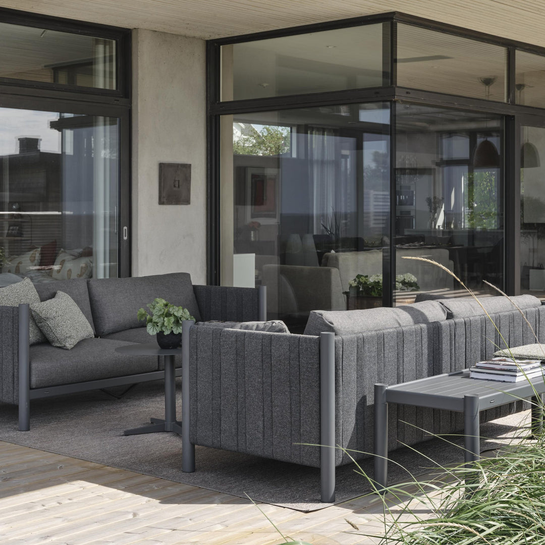 Brafab Brad sofabord i antrasitt på terrasse med mørk grå loungesofaer, prydgress og glassfasade bak