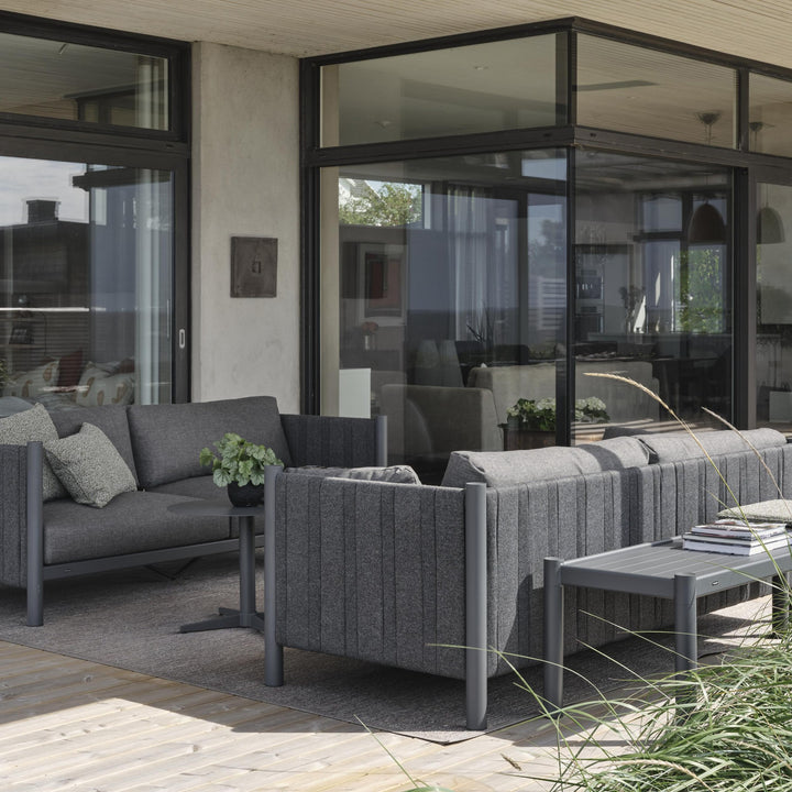 Brafab Brad sofabord i antrasitt på terrasse med mørk grå loungesofaer, prydgress og glassfasade bak