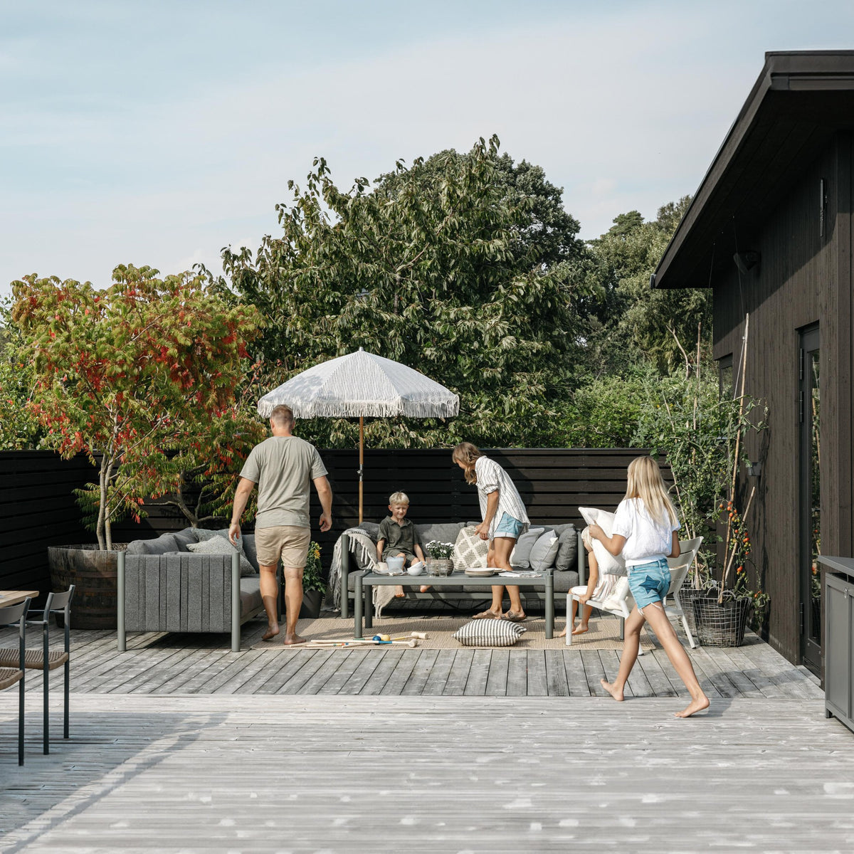 Brafab Brad sofabord i grønt på treterrasse med grå utesofa, parasoll og familie i hagen