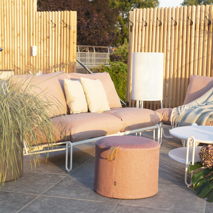 Kotte pall i rosa-rød tekstil foran beige utesofa på terrasse i kveldssol