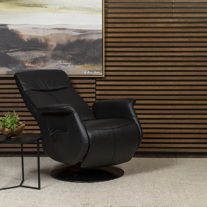Kiel reclinerstol i sort skinn, sett skrått i stue med panelvegg og sidebord med plante