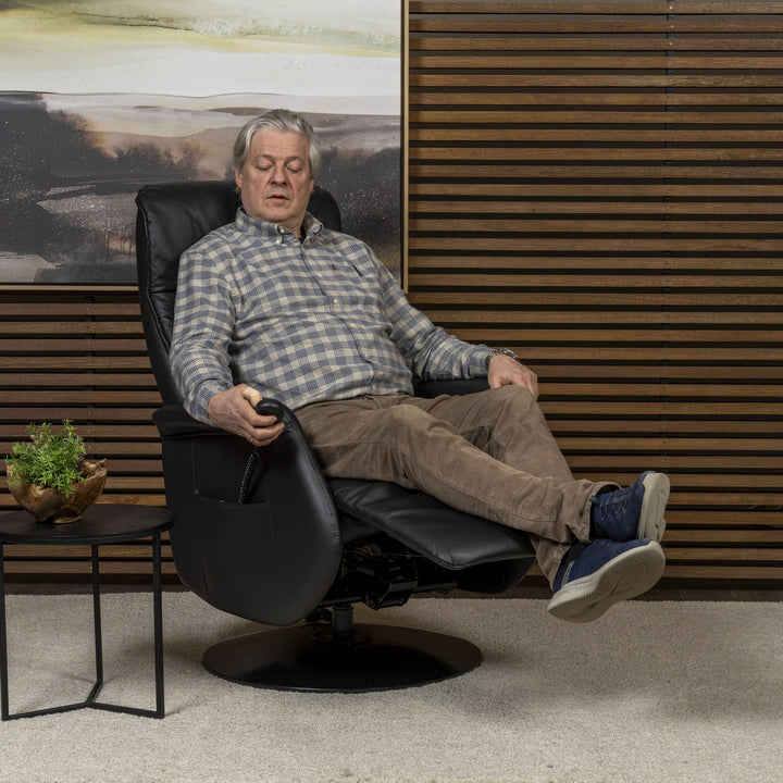 Kiel reclinerstol i sort skinn, mann sitter tilbakelent med beina oppe, stue med panelvegg og plante