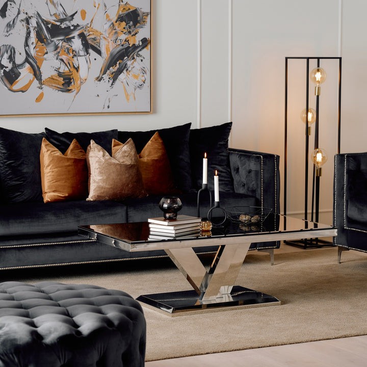 Messina sofabord med sort glassplate og blank V-base i stue med sort sofa og brune puter