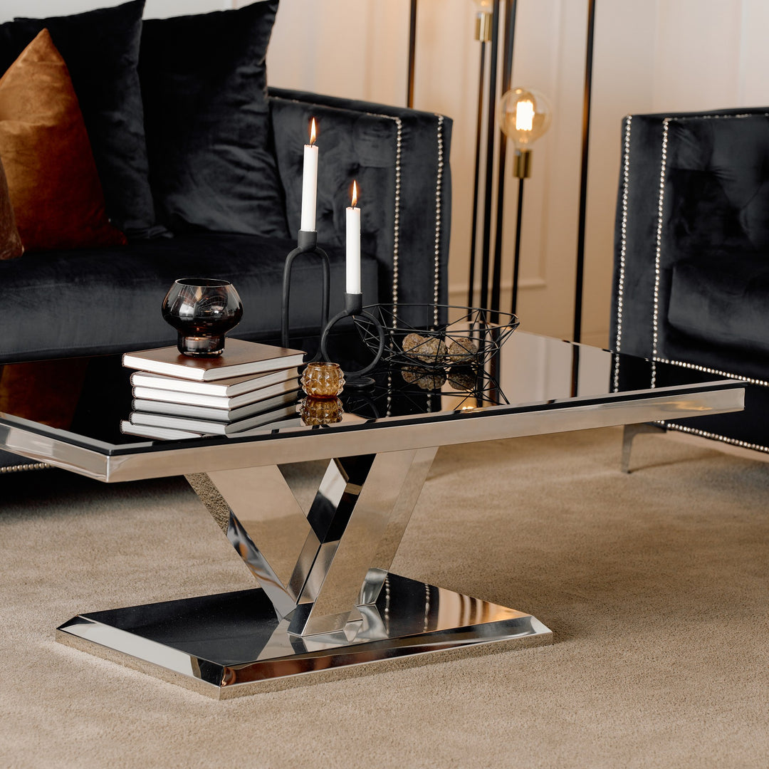 Messina sofabord med sort glassplate og V-formet krombase ved sort veloursofa
