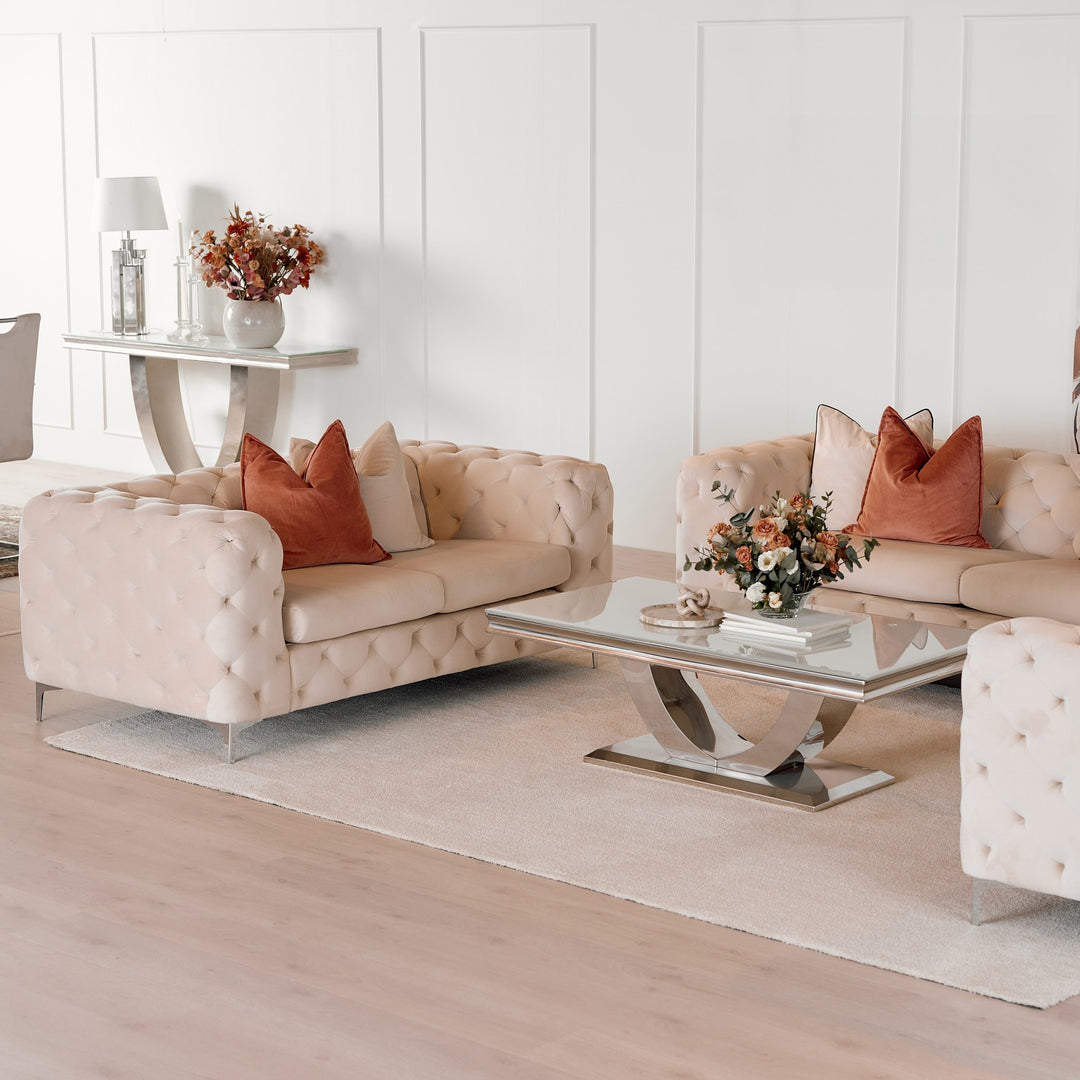 Firenze sofabord med lys glassplate og buet forkrommet fot, foran beige chesterfieldsofaer