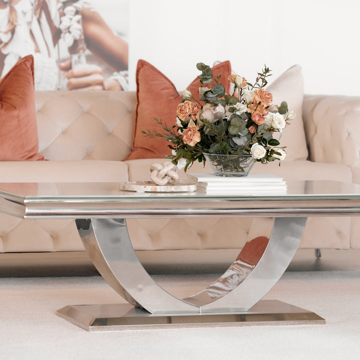 Firenze sofabord med lys glassplate og buet kromfot foran beige chesterfieldsofa med terrakottaputer