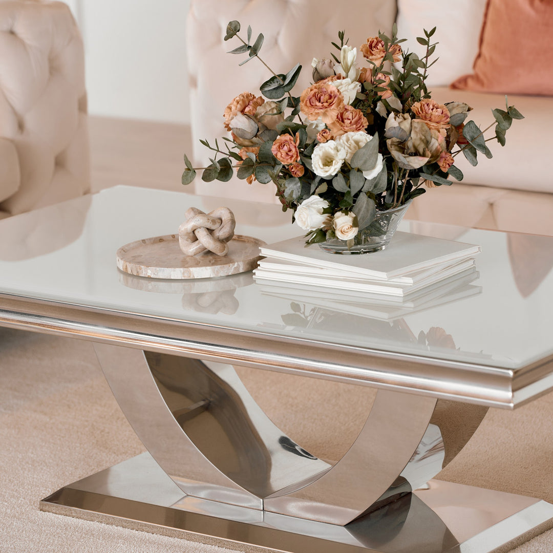 Firenze sofabord med lys glassplate og buet kromfot, pyntet med blomster foran beige sofa