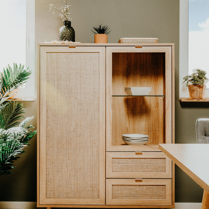 Bali highboard i lys eik med rottingdør og glasshylle med tallerkener, mot grønn vegg med grønne planter