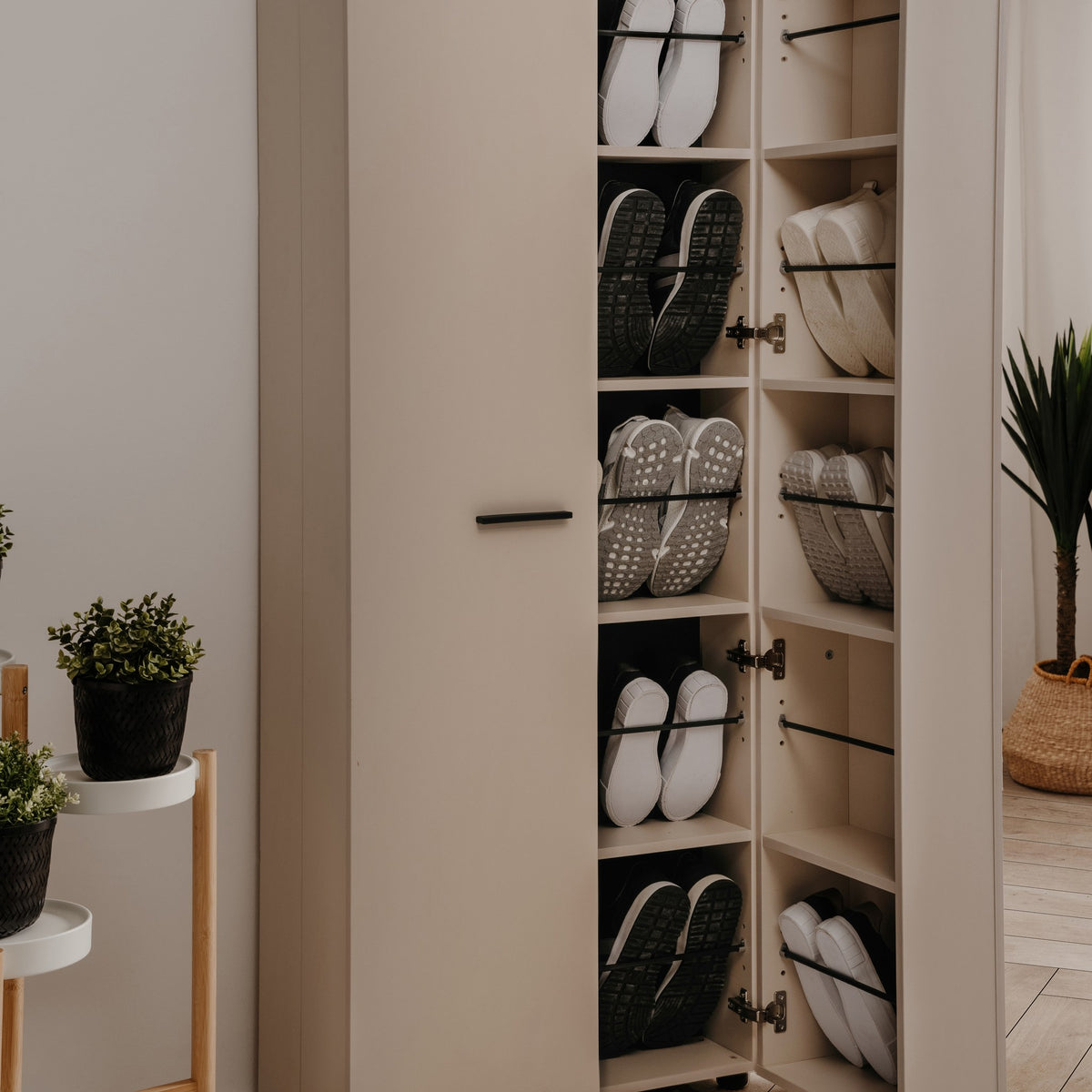 Satos skoskap i beige med åpen dør og flere skråhyller fulle av sko, i lyst rom med grønne planter