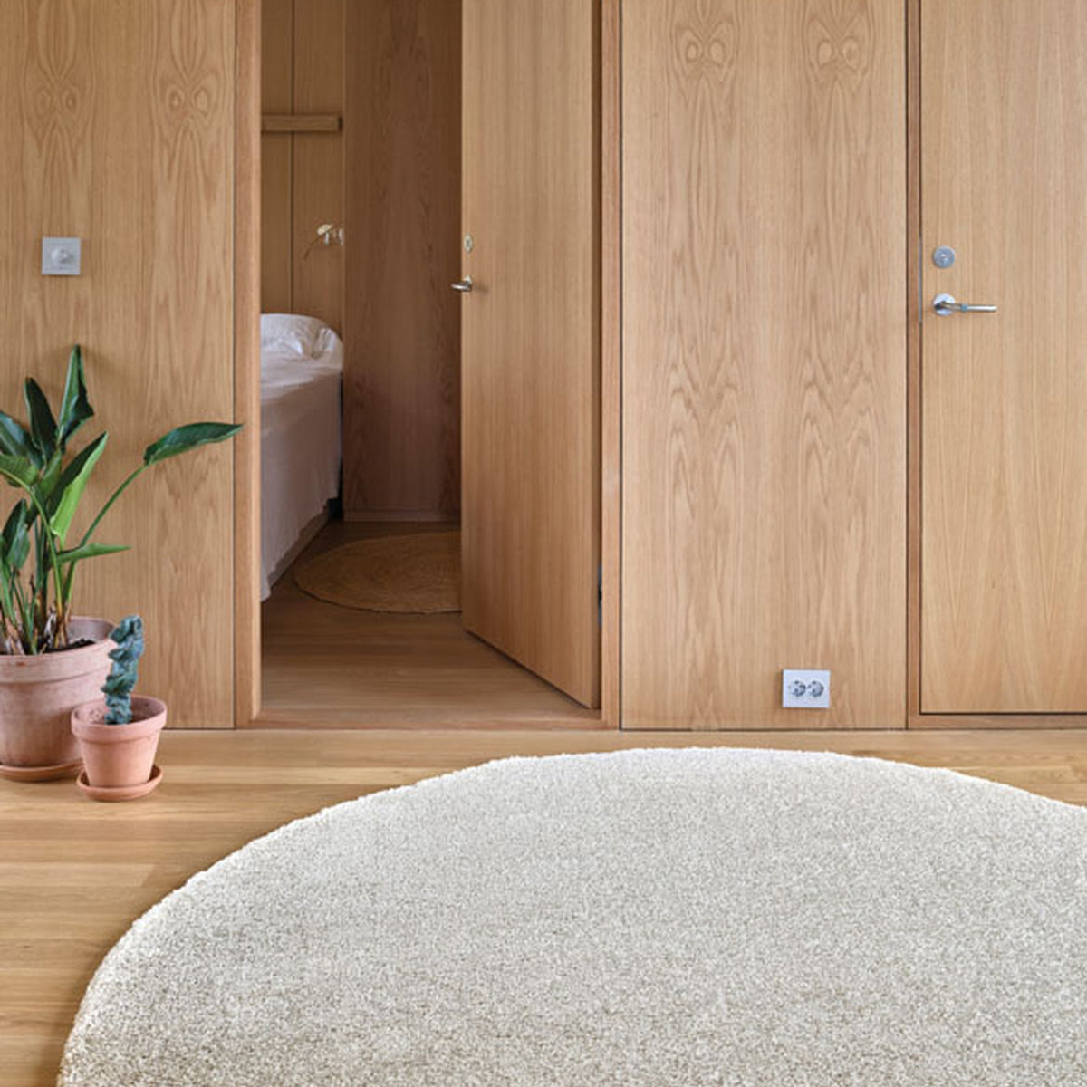 InHouse Spectrum teppe rundt i sand på tregulv i soverom med eikegarderobe og planter