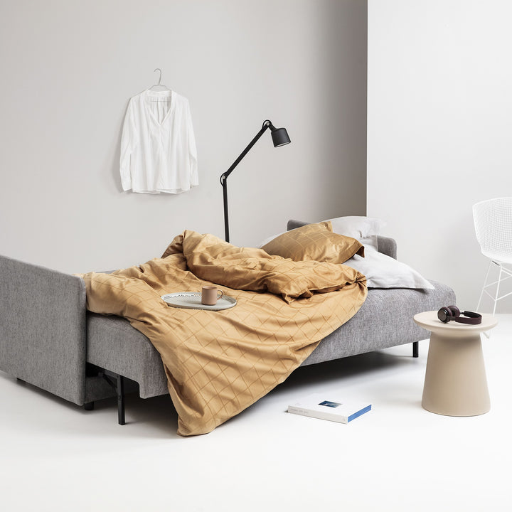 Hovden Flexy sovesofa i grå, redd opp som seng med okergult sengetøy og svart lampe