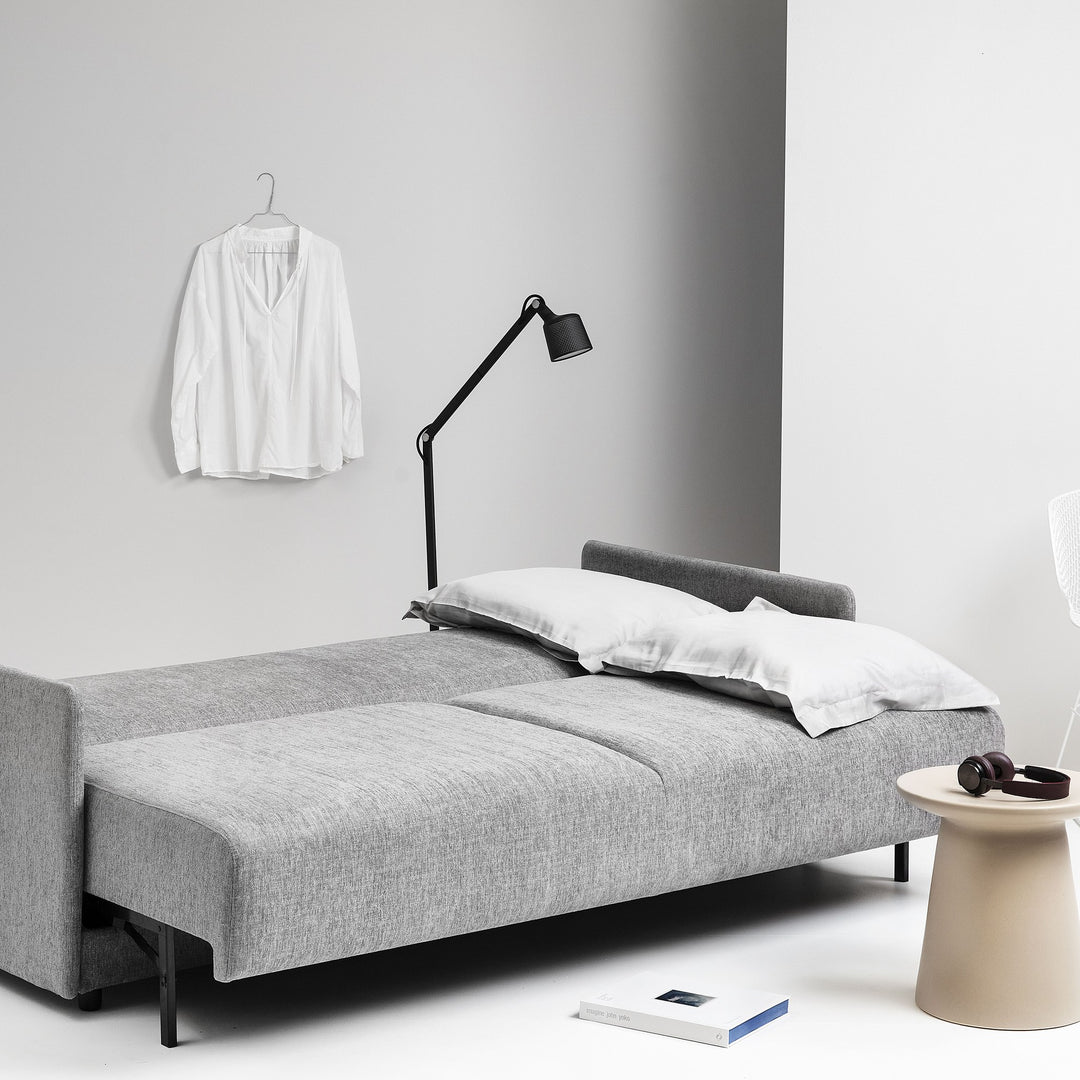 Hovden Flexy sovesofa i grå, utfelt til seng med grått sengetøy og svart gulvlampe