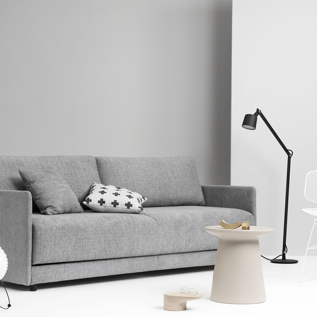 Hovden Flexy sovesofa i grå mot lys grå vegg med pute, sidebord og gulvlampe