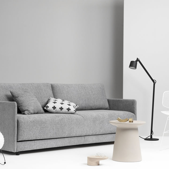 Hovden Flexy sovesofa i grå mot lys grå vegg med pute, sidebord og gulvlampe