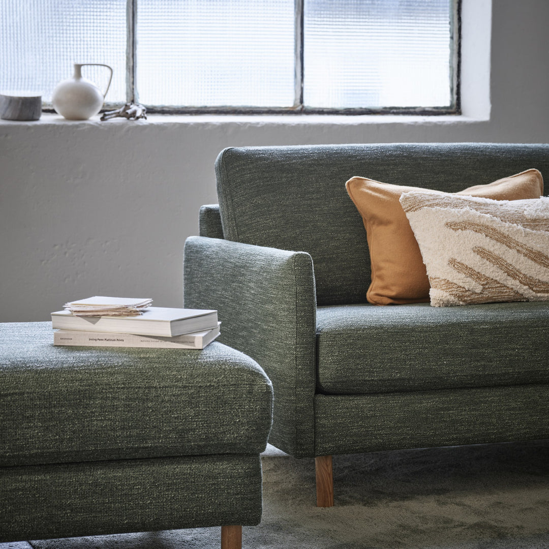 Scandinavian Touch 4-seter sofa i grågrønn chenille med cognac skinnpute og bøker, ved vindu med vase