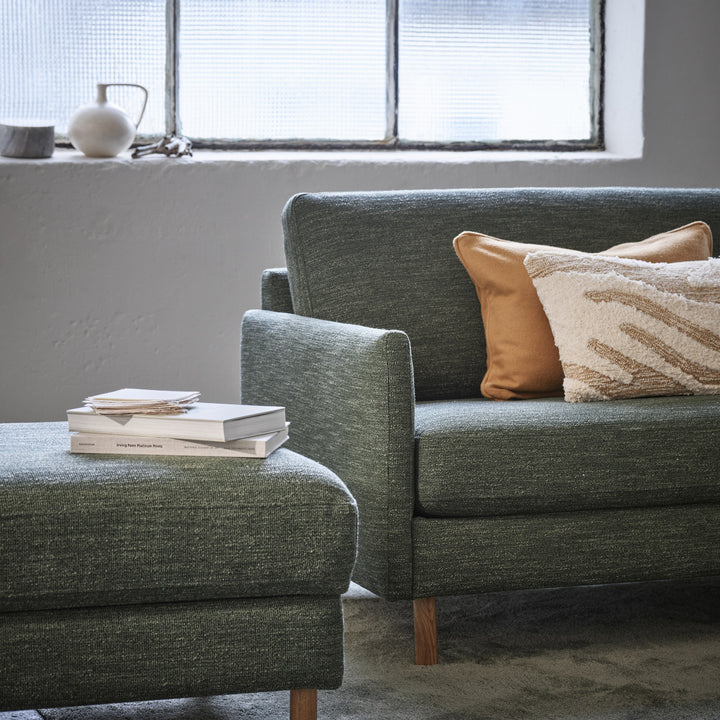 Scandinavian Touch 4-seter sofa i grågrønn chenille med cognac skinnpute og bøker, ved vindu med vase