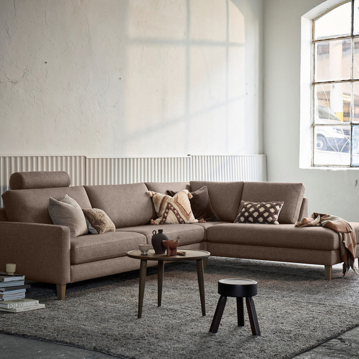 Hovden Scandinavian Touch nakkepute på gråbrun hjørnesofa i lyst rom med sofabord og pall.