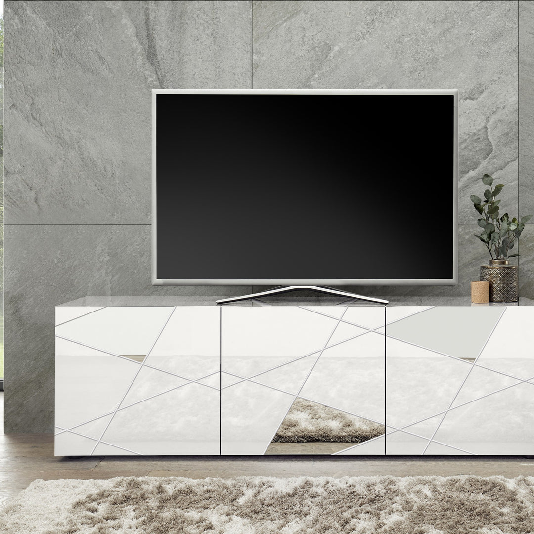 Vittoria TV-benk i hvit høyglans med fasettmønster, TV og plante mot grå steinvegg.