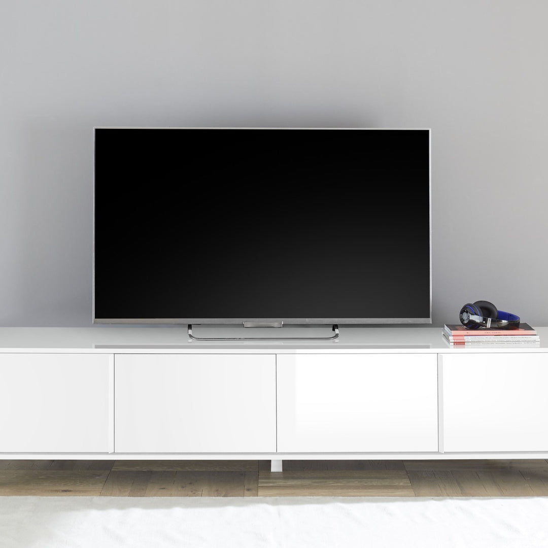 City TV-benk i hvit høyglans med TV, bøker og hodetelefoner mot lys grå vegg.